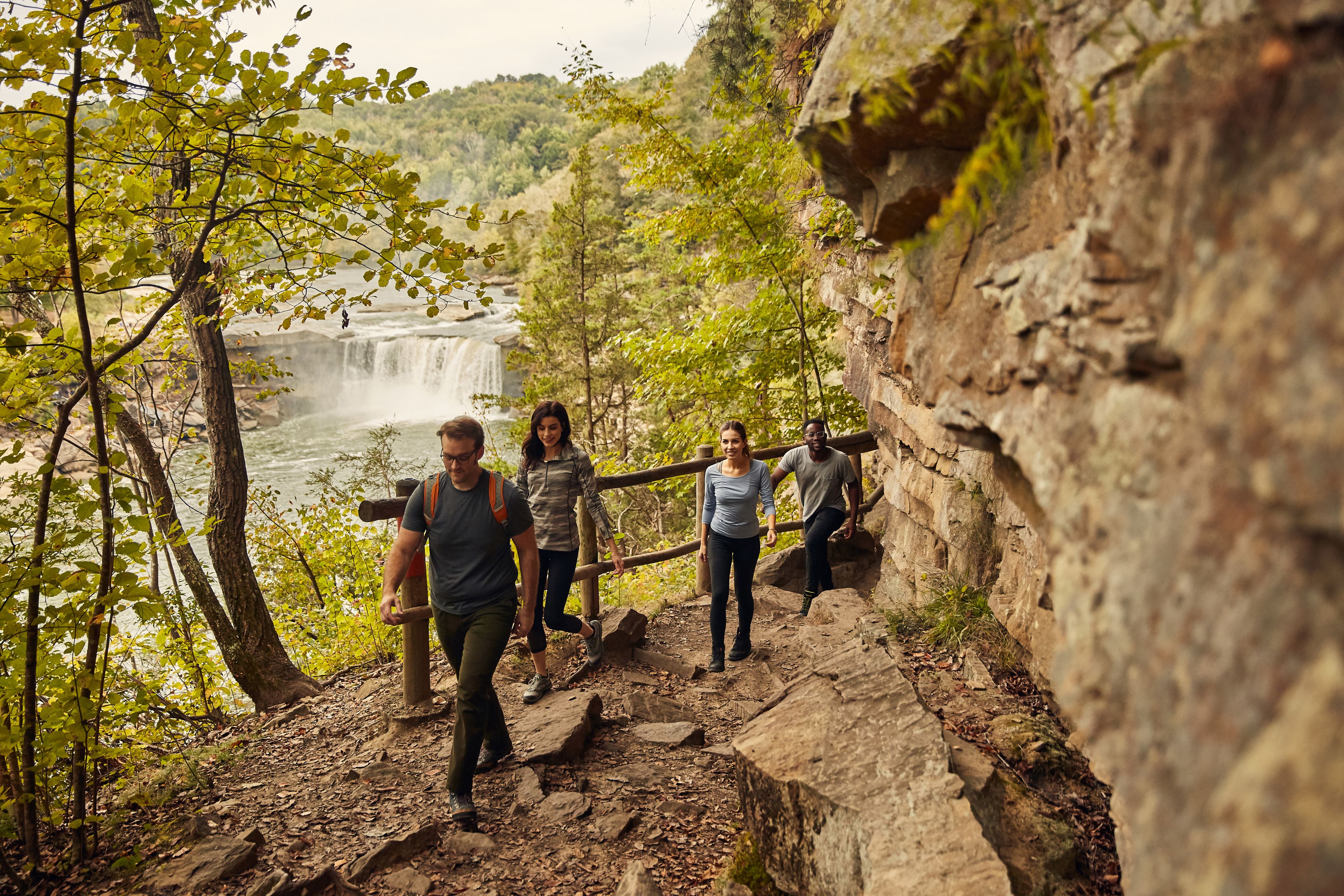 Un grupo de personas caminando por un sendero rocoso, con una cascada al fondo.