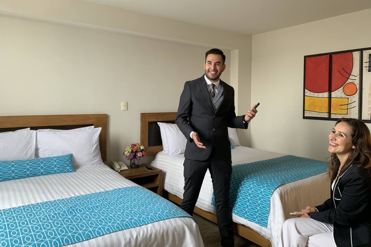 A hotel room with two beds, a nightstand with a phone and a vase of flowers, and a painting on the wall.
