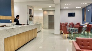 A hotel lobby with a reception desk, a dining area with tables and chairs, and a modern elevator. - Rymma Hotel (Morelia)