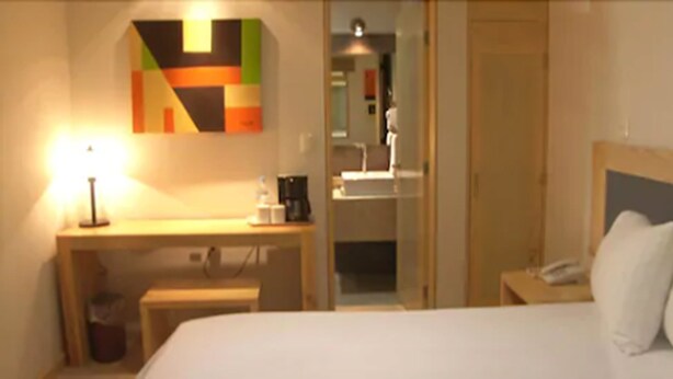 A hotel room with a bed, a desk, a lamp, a coffee maker, and a mirror. - Rymma Hotel (Morelia)