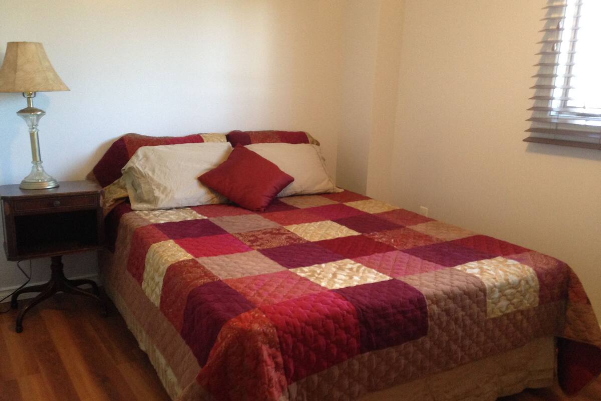 A bedroom with a bed, a nightstand, a lamp, and a window with blinds.