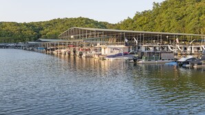 A marina with boats docked, a covered boat ramp, and a forested hillside in the background.