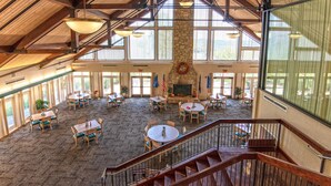 A spacious indoor area with multiple tables and chairs, a stone fireplace, and large windows allowing natural light.