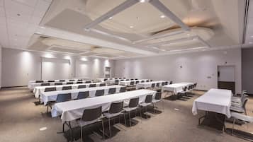 A conference room with multiple tables and chairs, white walls, and a carpeted floor.