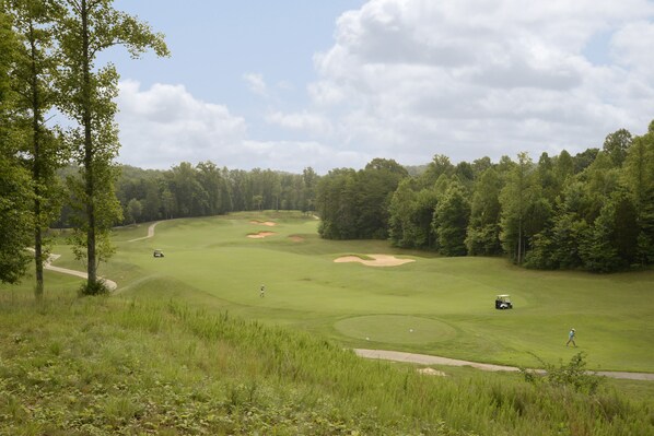 Un campo de golf con bunkers de arena, un sendero para peatones y un carrito de golf.