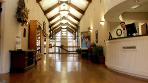 A hotel lobby with wooden floors, a reception desk, a staircase, and a large window allowing natural light.