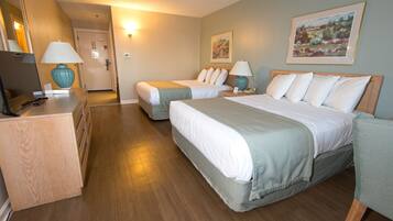 A hotel room with two beds, a desk with a lamp, a mirror, and a painting on the wall.