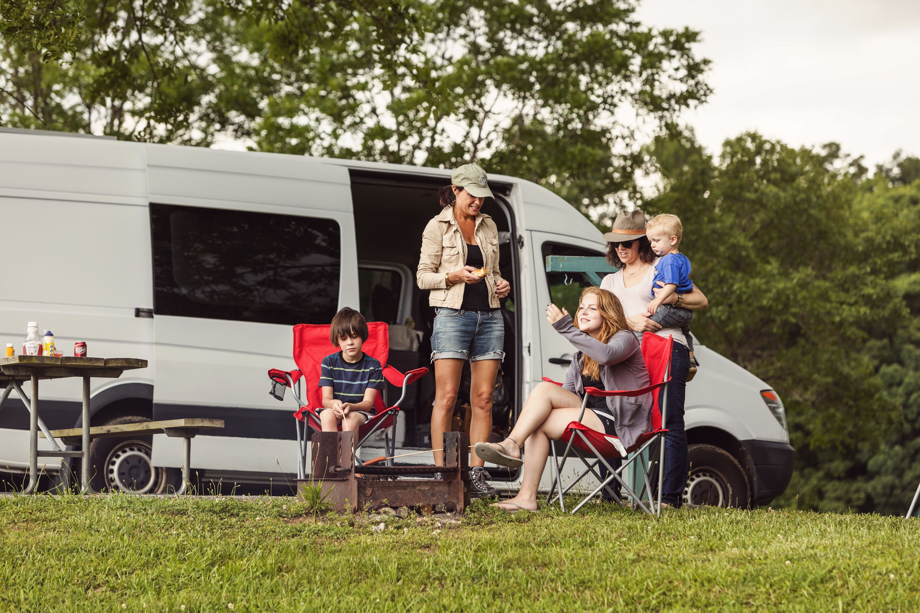 Una familia acampando con una furgoneta, sillas de exterior y una mesa de picnic.