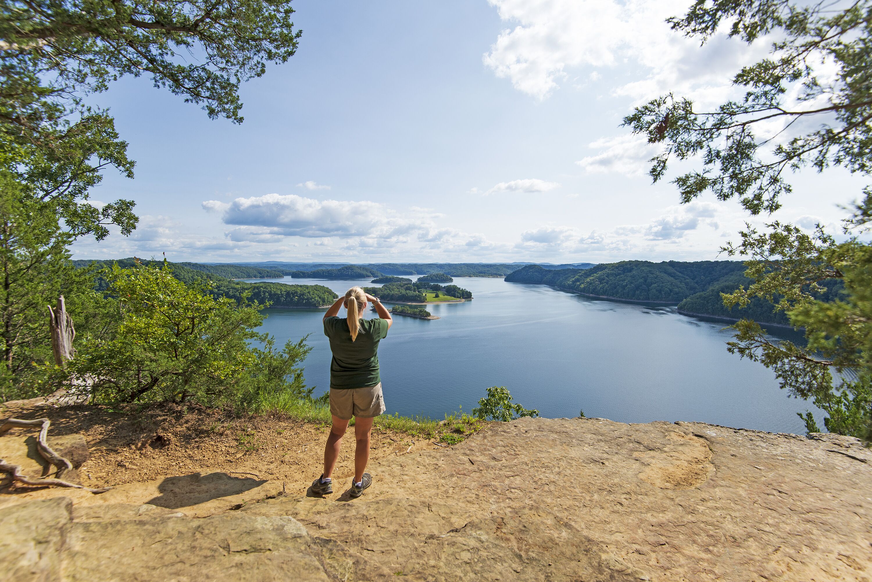 A person standing on a rocky outcrop overlooking a lake surrounded by hills.
