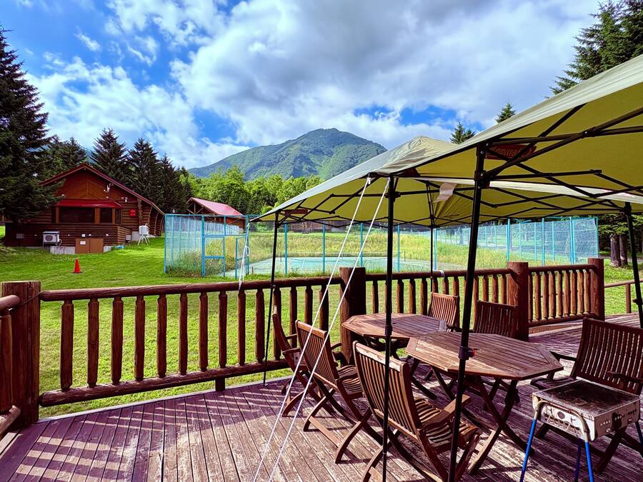 A wooden deck with outdoor seating and a covered area, overlooking a grassy area with a mountain in the background.