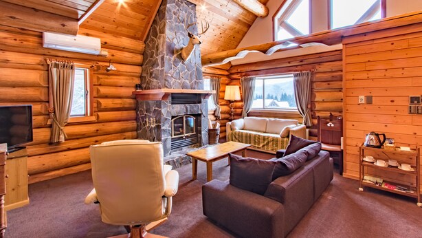L’intérieur d’une cabane en rondins, avec une cheminée en pierre, des meubles en bois et un téléviseur.