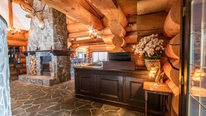 L’intérieur d’une cabane en rondins, avec une cheminée en pierre, des poutres en bois au plafond et un sol en pierre.