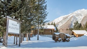 Une cabane en bois portant l’inscription « Villa Rusutsu », entourée d’arbres et de montagnes couverts de neige.