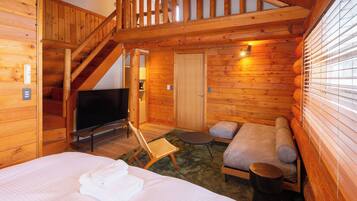 A wooden cabin with a loft bedroom, a sofa bed, a small table, and a TV.