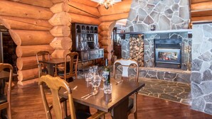 L’intérieur d’une cabane en rondins, avec une cheminée en pierre, une table à manger en bois et des chaises.