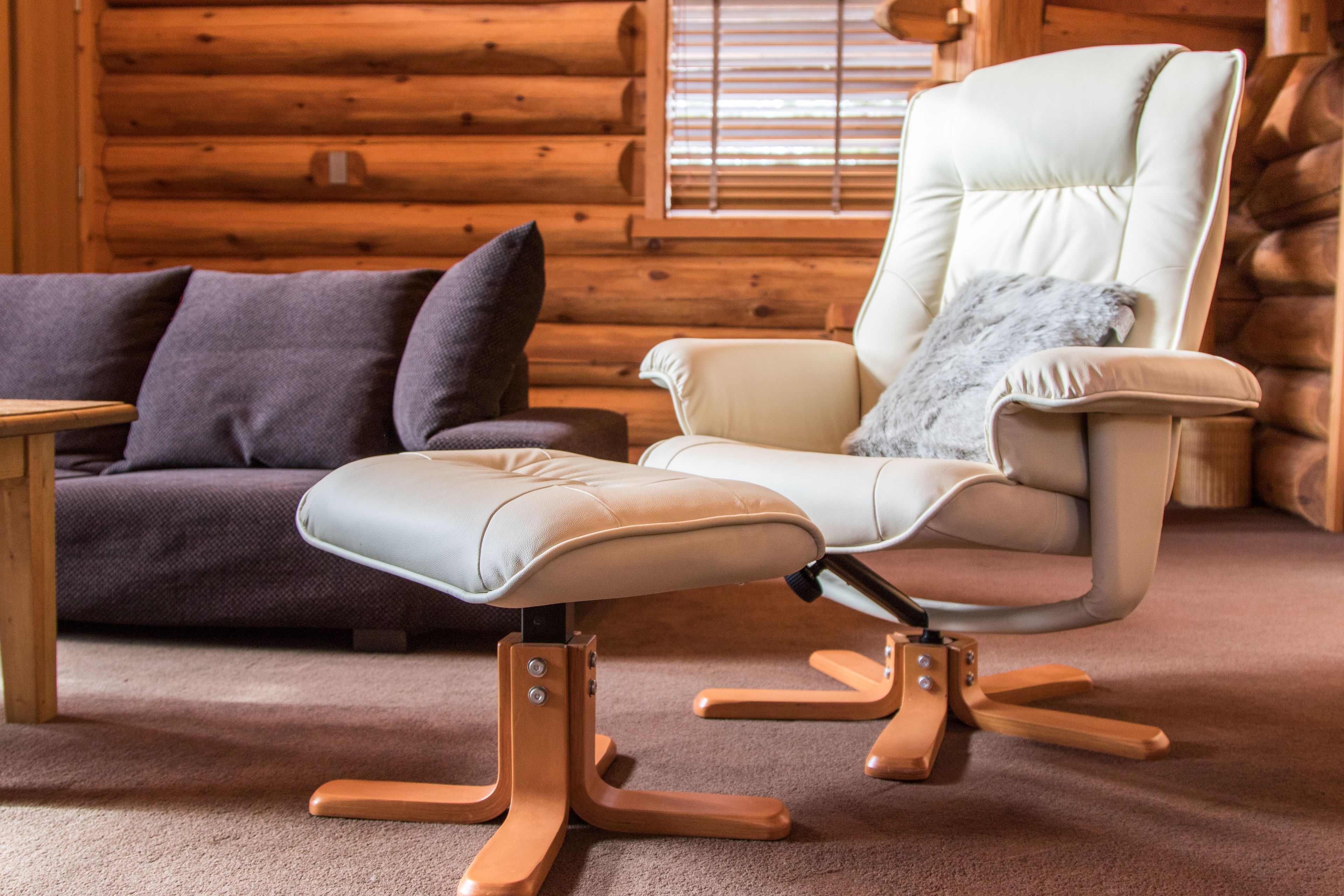 A modern log cabin interior with a beige leather sofa, a light-colored armchair with a fur throw, and a wooden coffee table.