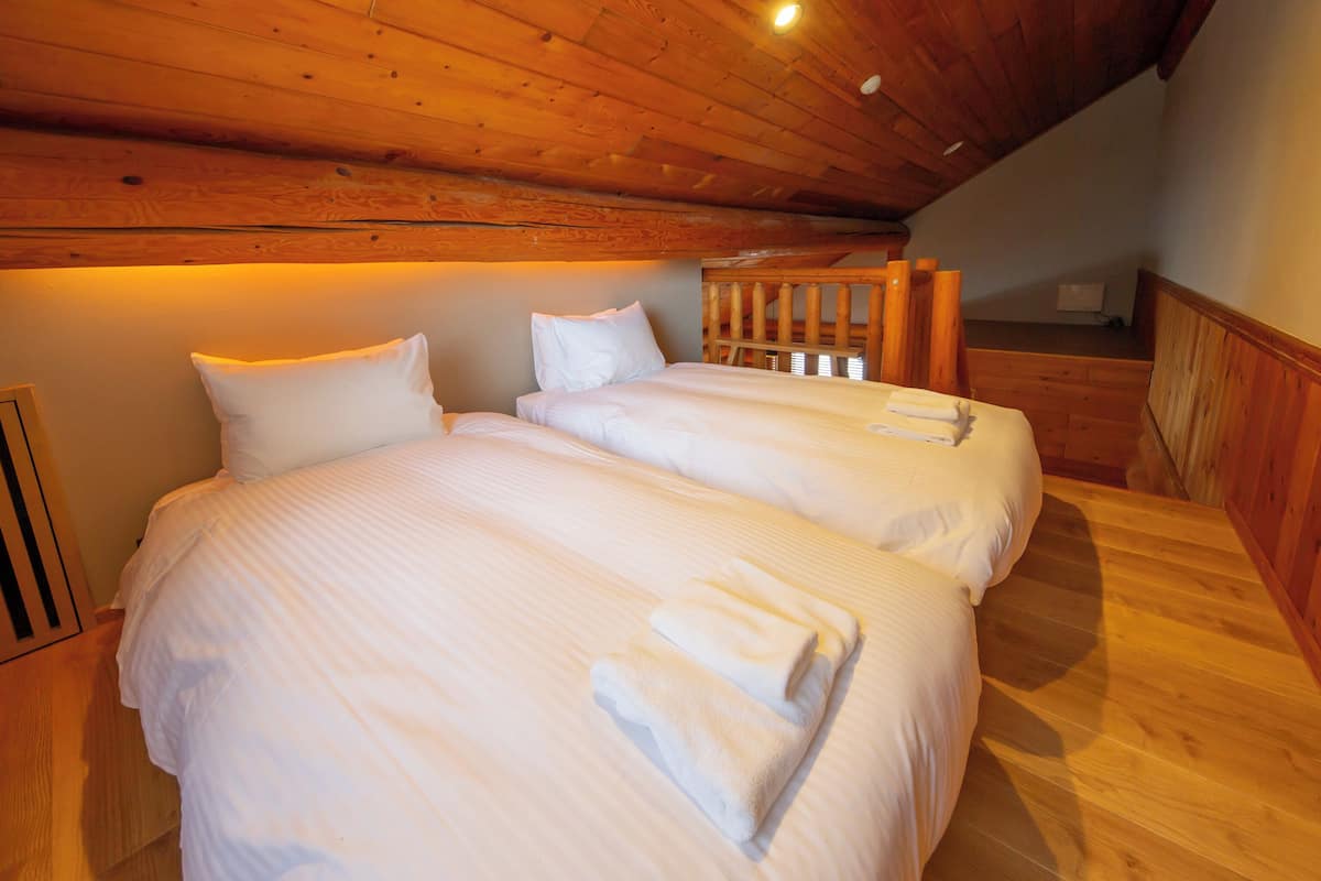 Ein Zimmer mit zwei Betten, Holzboden und schrägverdeckter Decke.