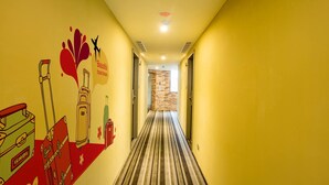 A hotel hallway with striped carpet, yellow walls, and a mural of luggage and travel-related icons. - Just Live Inn Keelung (Keelung)