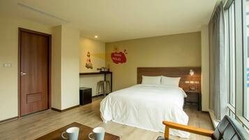 Quarto de hotel com cama, escrivaninha, cadeira e janela.