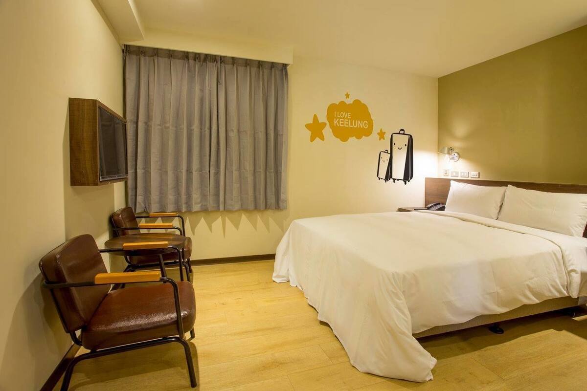 A hotel room with a bed, a desk with chairs, a television, and a wall decoration.