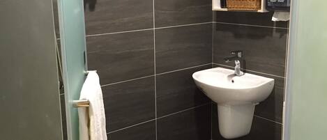 Un baño moderno con baldosas oscuras, un lavamanos blanco y un inodoro.