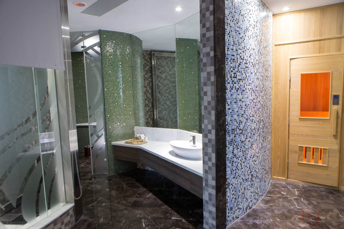 Een moderne badkamer met een douche met glazen wand, een witte wastafel en wandtegels in mozaïek.