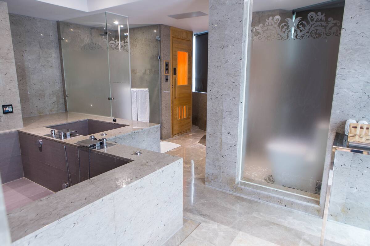 Een moderne badkamer met een groot marmeren wastafel, een douche met glazen wanden en een houten deur.