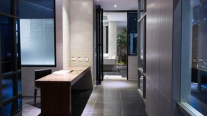 A modern hotel corridor with a wooden reception desk, a glass wall, and a view into a bathroom with a sink and a plant. - All-Ur Boutique Motel - Tai-Tung Branch (Taitung)