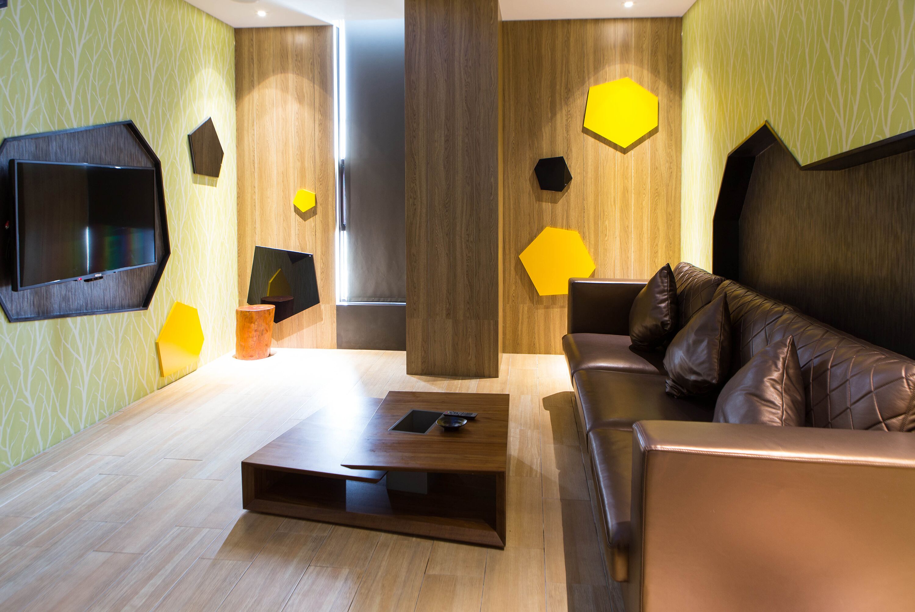 A modern living room with a wooden floor, a leather sofa, a coffee table, and a flat-screen TV mounted on the wall.