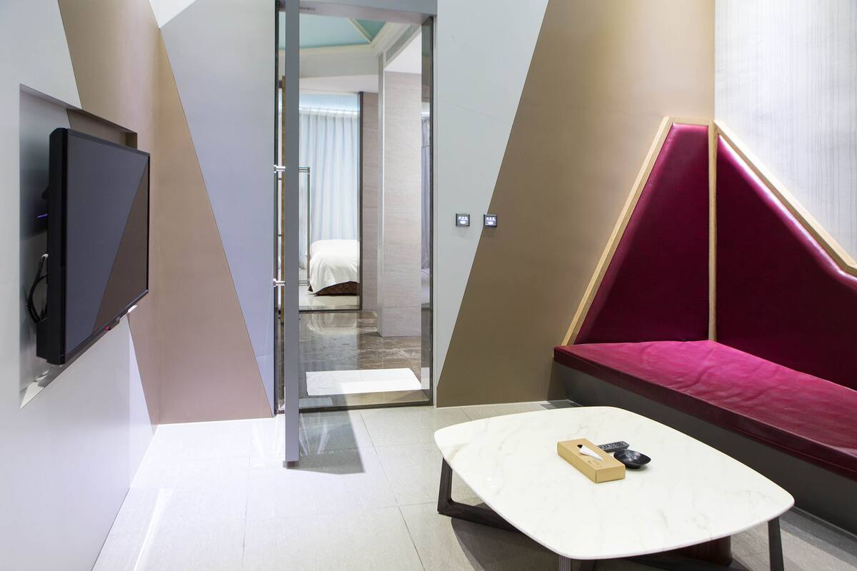 Een moderne hotelkamer met een flatscreen televisie, een witte marmeren tafel en een rode, beklede bank.