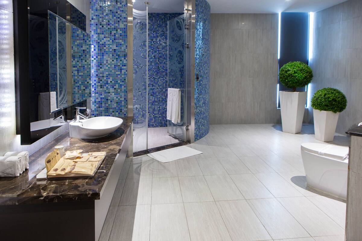 Een moderne badkamer met een groot wastafelmeubel, een douchecabine met glazen wanden en twee potplanten.