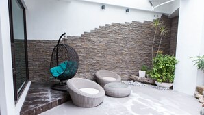 A modern outdoor seating area with wicker chairs and ottomans, a hanging chair, and a stone wall backdrop. - All-Ur Boutique Motel - Tai-Tung Branch (Taitung)