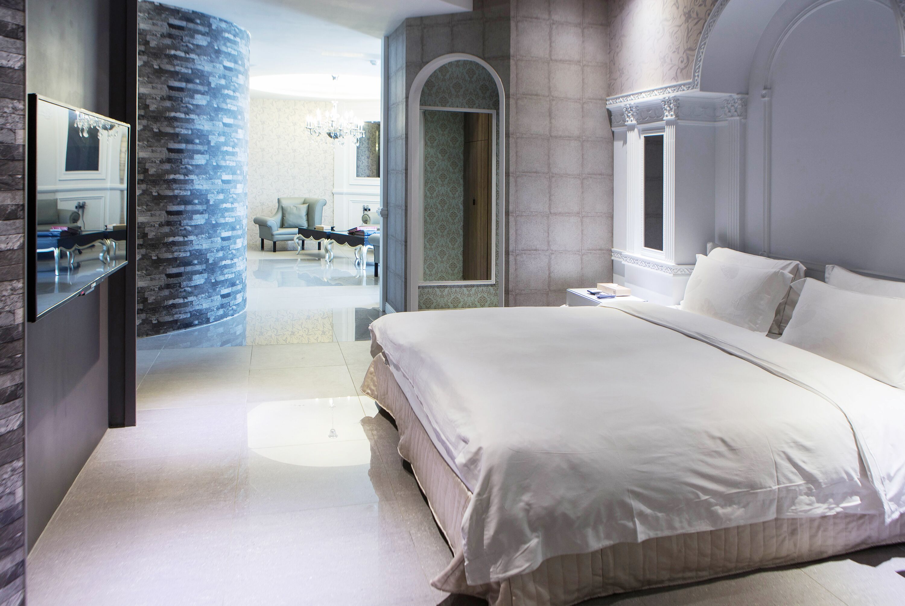 A modern bedroom with a large bed, a mirror, and a stone accent wall.