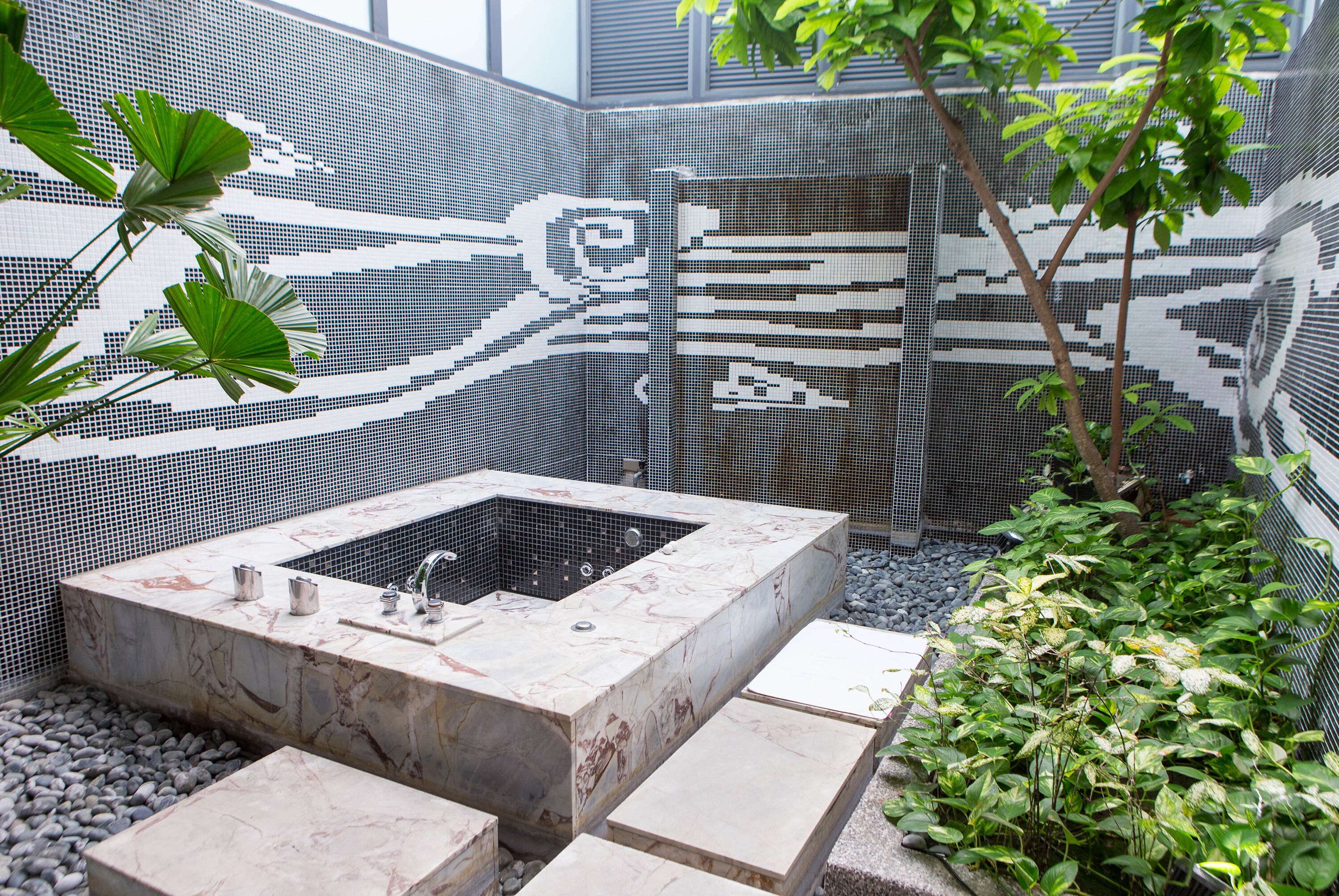 A modern outdoor bathroom with a marble sink, a large window, and a mosaic wall.