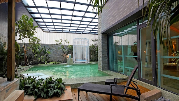 A modern outdoor pool area with a glass enclosure, a seating area with a chair, and a stone wall. - All-Ur Boutique Motel KaoHsiung Branch (Kaohsiung)