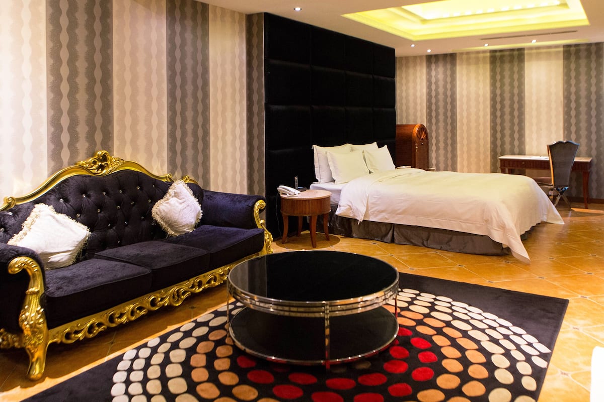 Una habitación de hotel con una cama grande, un sofá, una mesa de centro redonda y un escritorio.