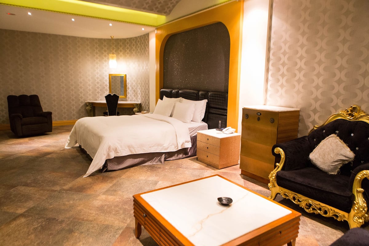 Una habitación de hotel con cama, mesita de noche, sillón, sofá y una pequeña mesa.