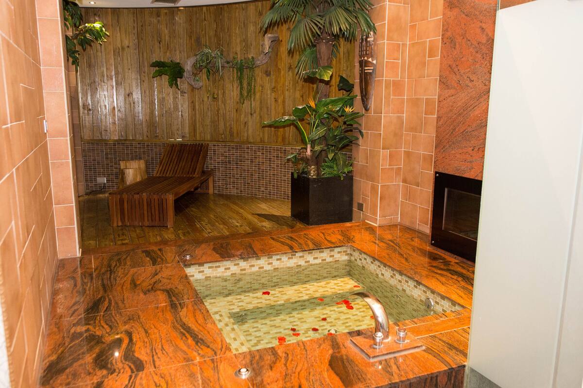 Un baño con pared de madera, una banca, una planta en maceta y suelo de baldosas.