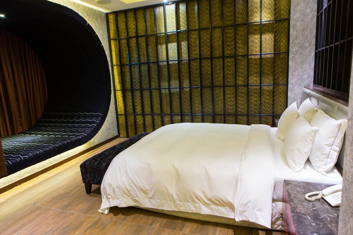 Een hotelkamer met een bed, een bankje, een telefoon en een behang met patroon.
