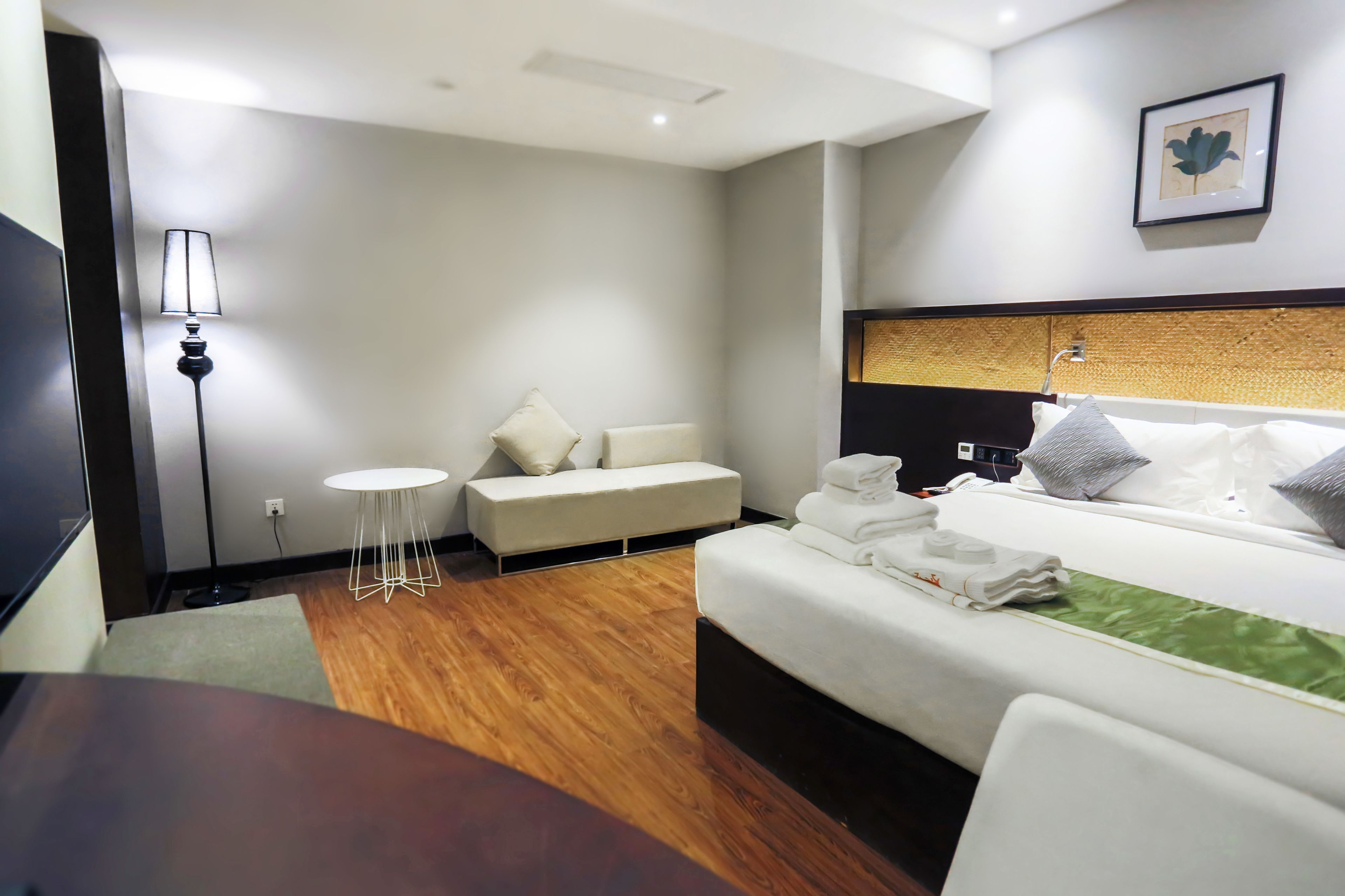 A hotel room with a bed, a sofa, a small round table, and a floor lamp.
