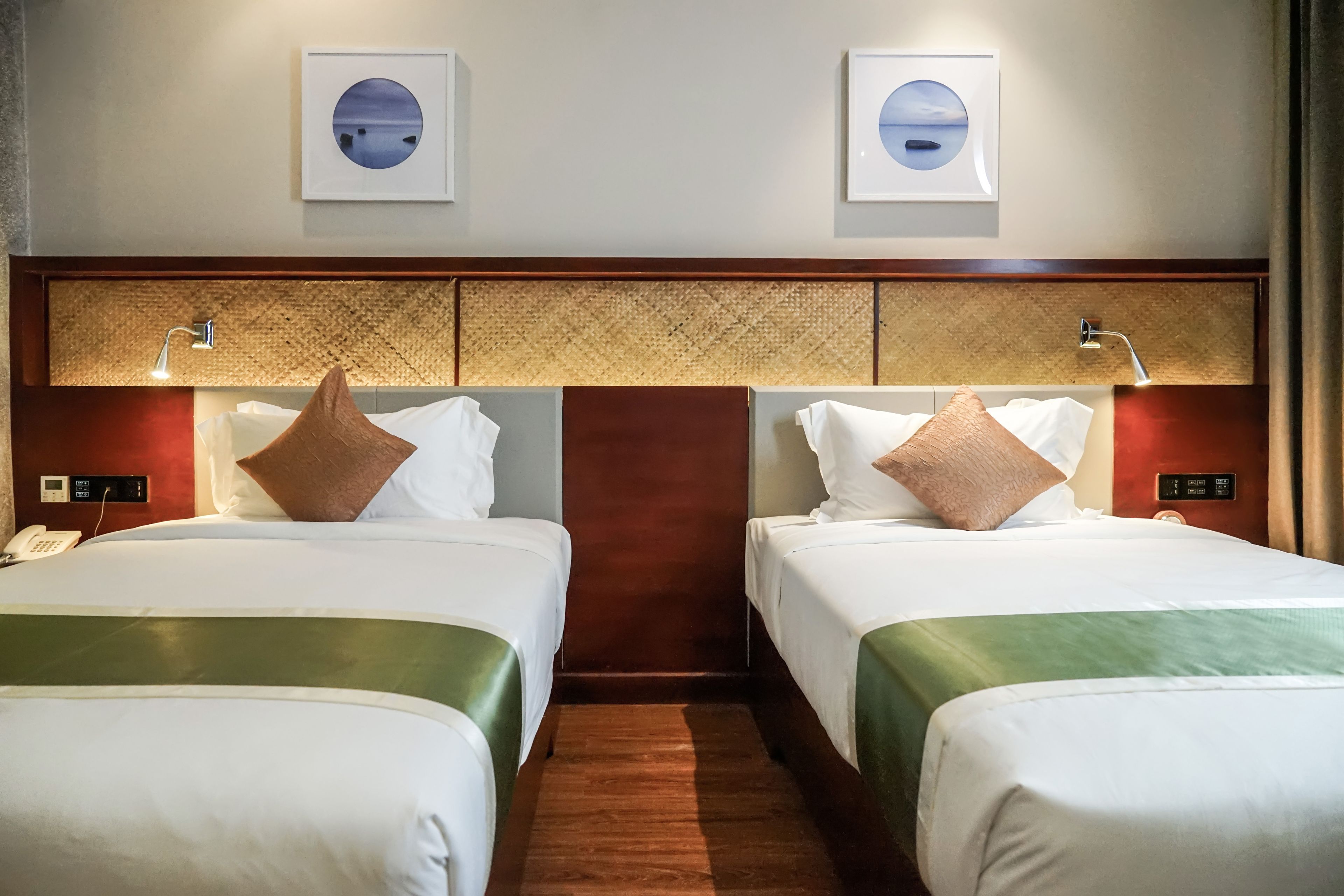A hotel room with two single beds, a wooden headboard, a phone, and framed artwork on the wall.