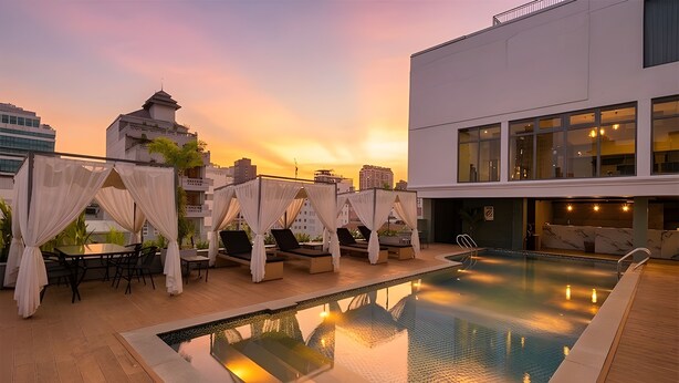 A rooftop pool with lounge chairs and a table, surrounded by buildings.