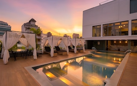 A rooftop pool with lounge chairs and a table, surrounded by buildings.