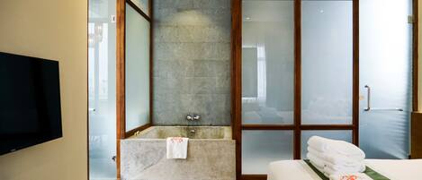 A modern hotel bathroom with a bathtub, a glass shower enclosure, and a neatly made bed with towels.