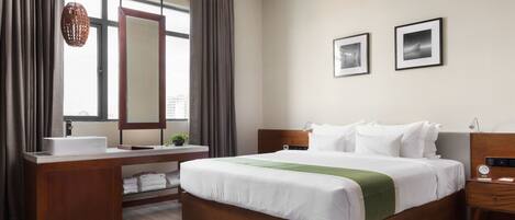 A hotel room with a wooden bed, a bedside table, a nightstand, a window with curtains, a mirror, and two framed pictures on the wall.