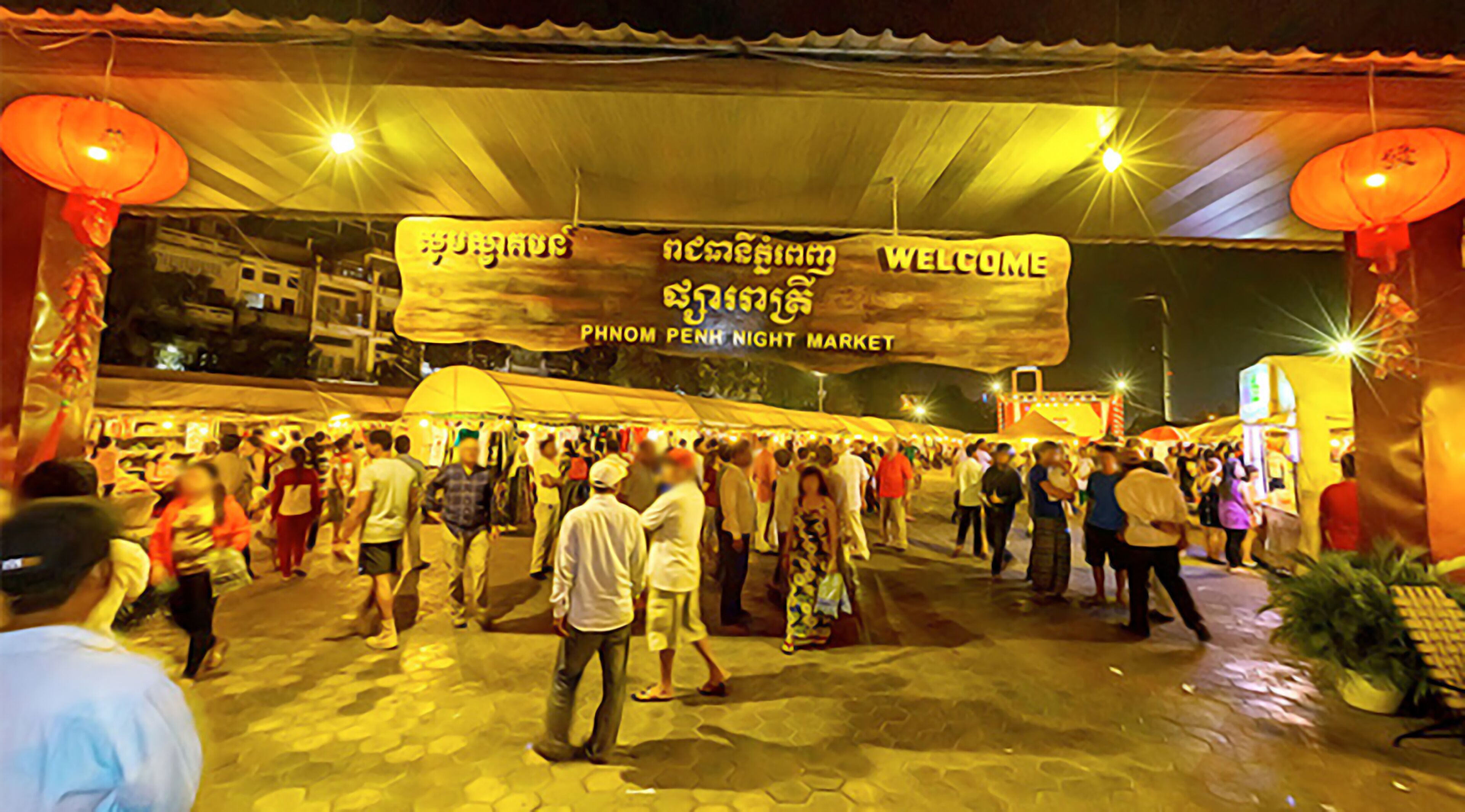 A crowded night market with a large welcome banner.