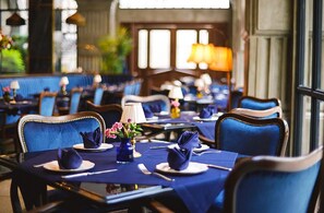 A restaurant with blue upholstered chairs, round tables, and a warm ambient light. - The Gunawarman (Jakarta)