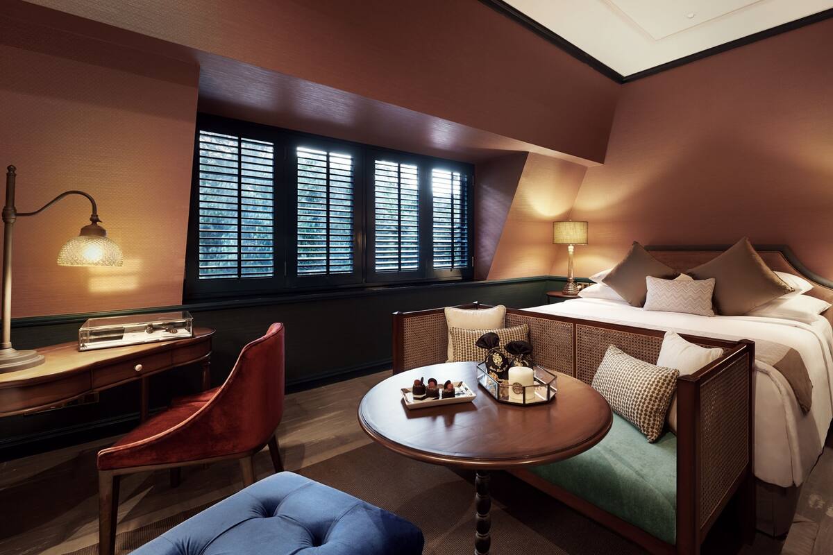 A hotel room with a bed, a desk, a chair, a table, and a window with blinds.