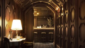 A narrow hallway with a patterned carpet, wooden walls with geometric designs, and a table with a lamp and chairs. - The Gunawarman (Jakarta)