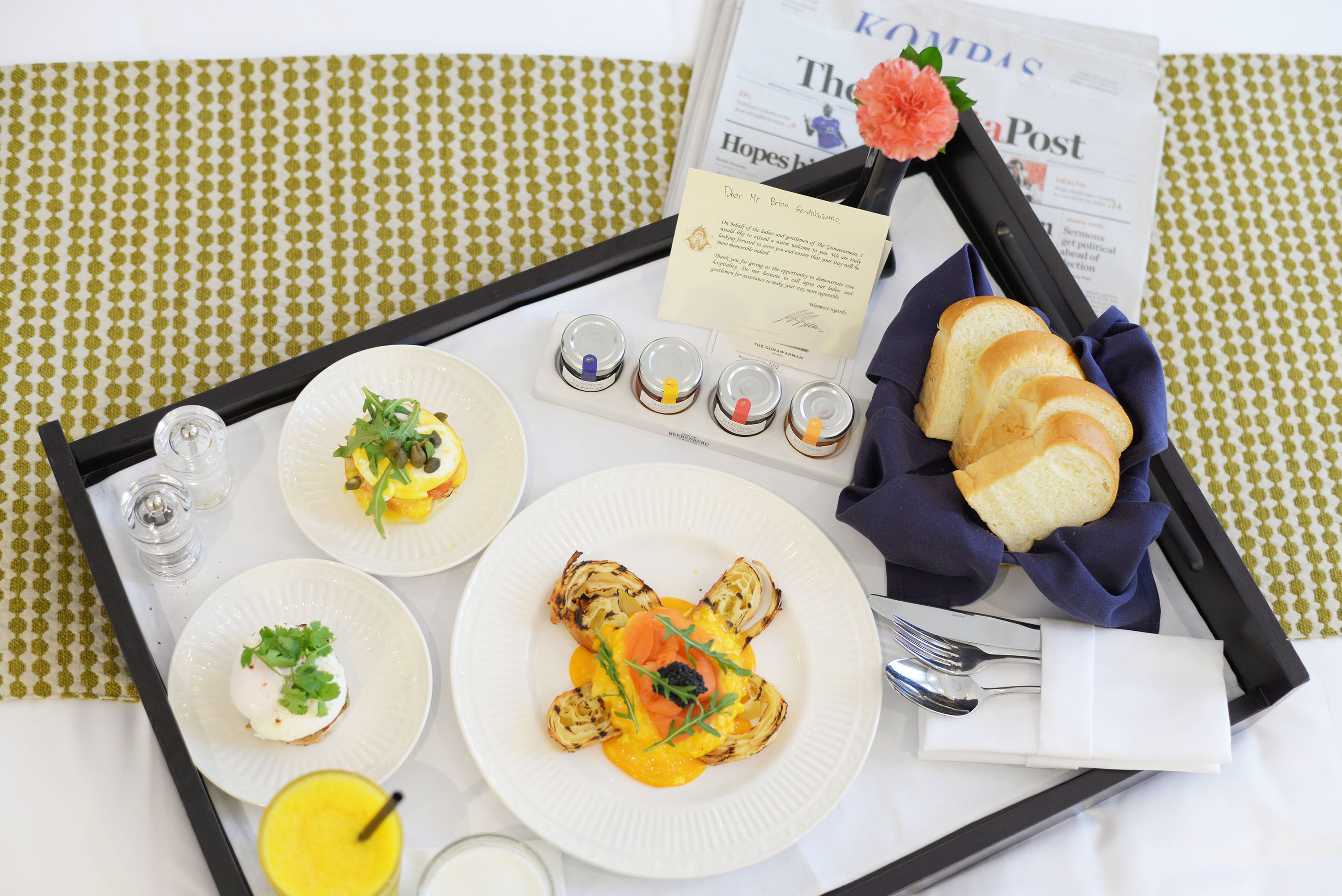 A breakfast tray with various dishes, a newspaper, and a card.